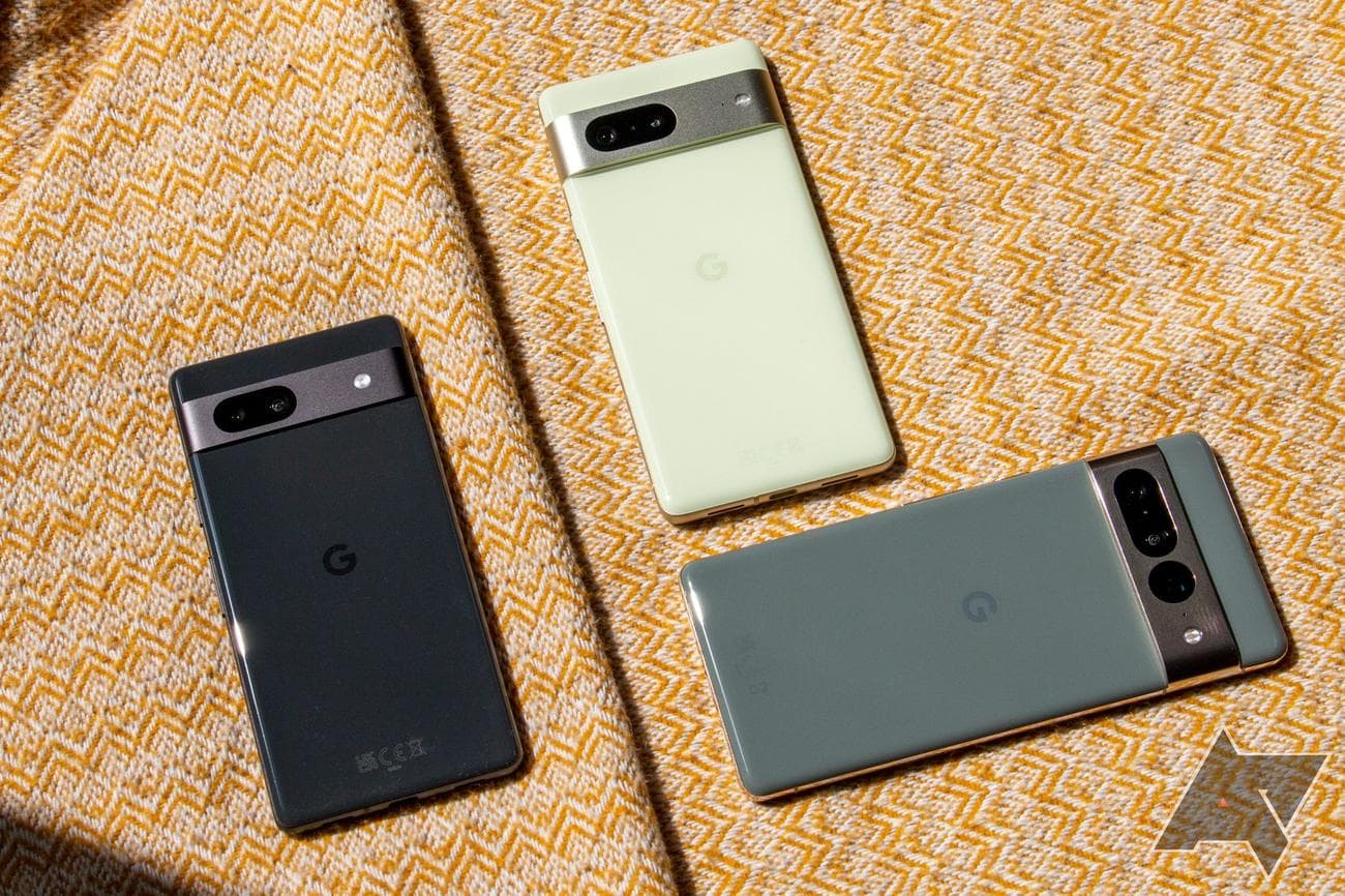 Google Pixel 7a, Pixel 7, and Pixel 7 Pro artistically arranged on a yellow sheet.