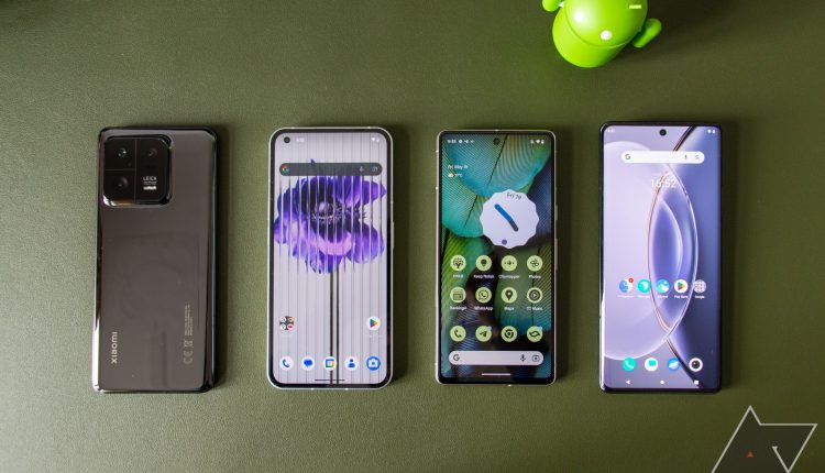 Four phones lie next to each other in a row, one face down and three face up with displays turned on, showing the home screen