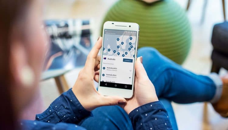 A person in a blue shirt and denim holds a phone with a VPN app open. 