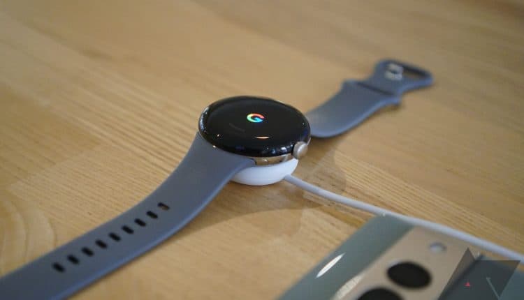 A smartwatch charging on a desk next to a smartphone.
