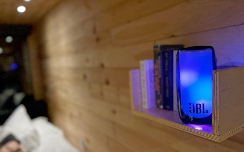 JBL Pulse 5 Bluetooth speaker pulsing blue in a getaway cabin