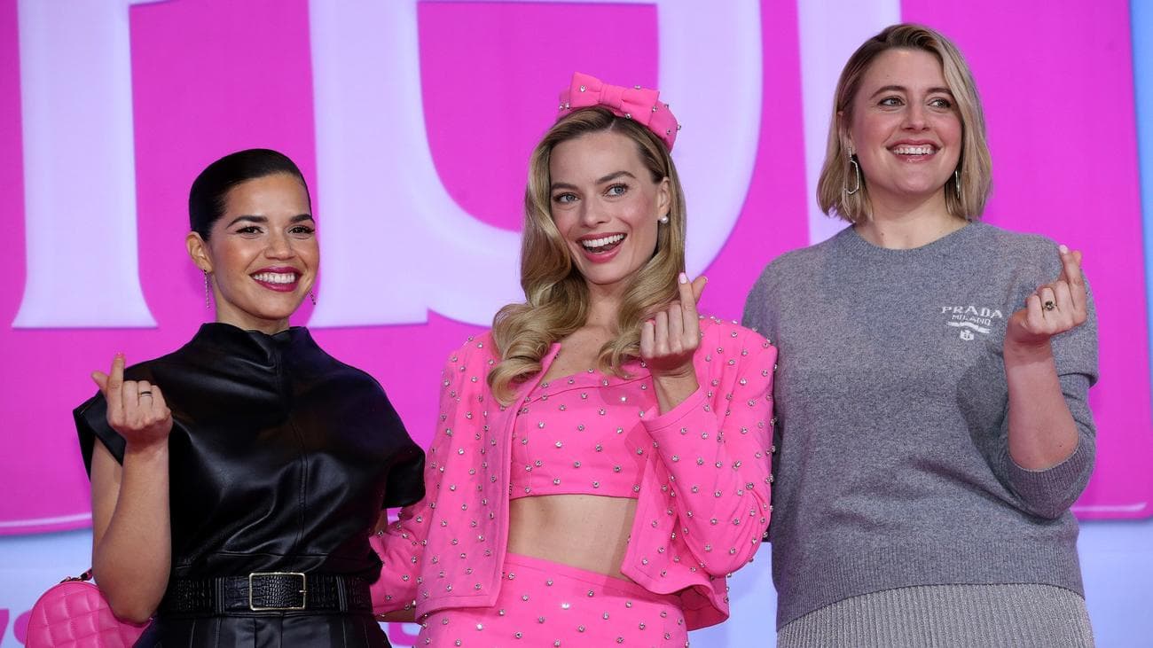 Τρεις γυναίκες ποζάρουν ενώ κάνουν καρδιές με τα δάχτυλα σε μια εκδήλωση στο κόκκινο χαλί. 