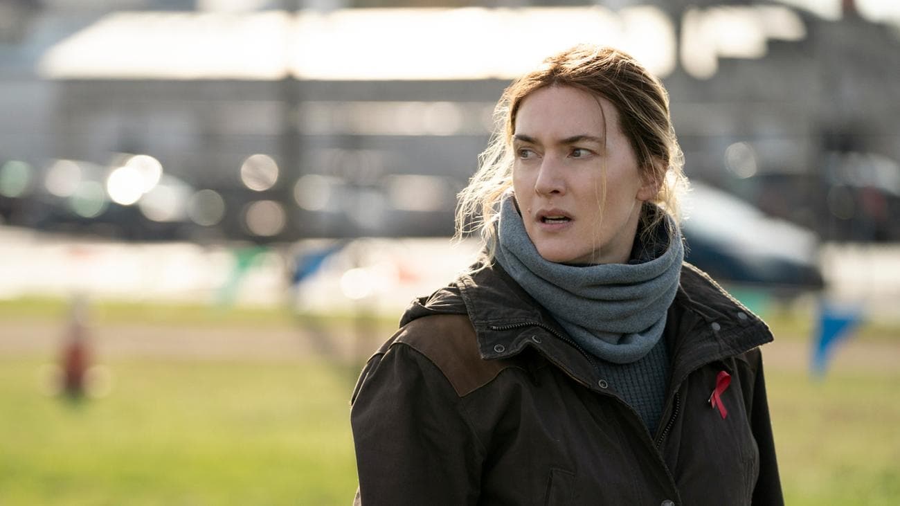 A woman in a jacket and scarf looks concerned.