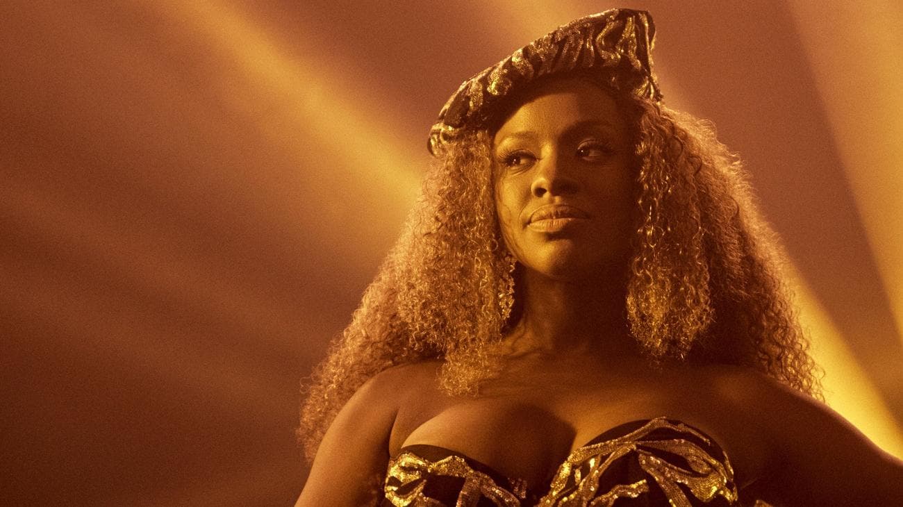 Μια γυναίκα που φοράει χρυσά ρούχα στέκεται σε μια σκηνή. 