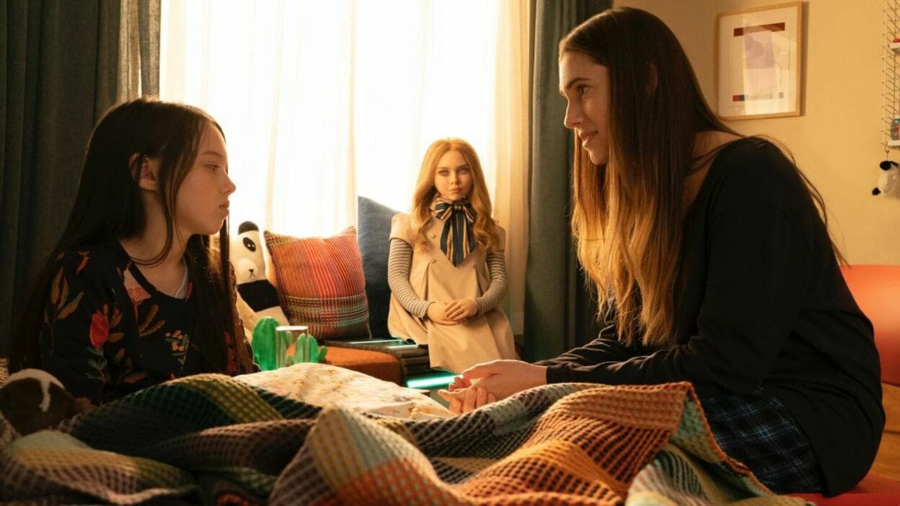 Μια γυναίκα μιλά σε ένα νεαρό κορίτσι ενώ κάθεται στην κρεβατοκάμαρά της.  Ανάμεσά τους κάθεται μια κούκλα.