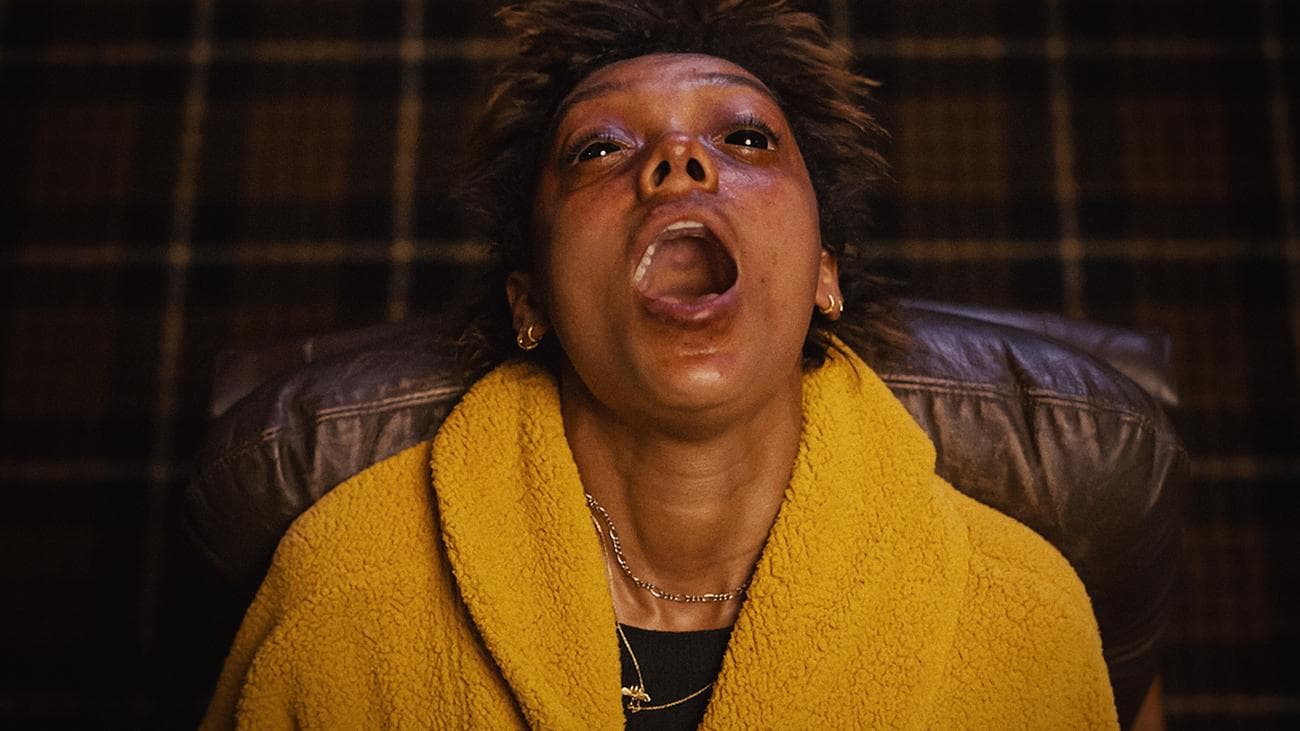 Μια γυναίκα που φορά ένα κίτρινο σακάκι ουρλιάζει ενώ κάθεται σε μια καρέκλα. 