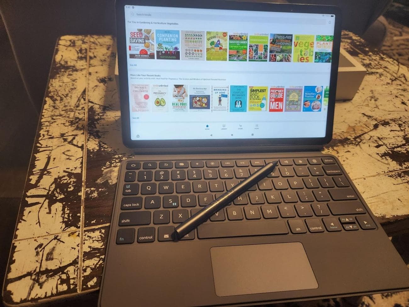 amazon tablet ανοιχτό στην εφαρμογή Kindle.  Έχει ένα πληκτρολόγιο προσαρτημένο με μια γραφίδα που κάθεται στο πληκτρολόγιο