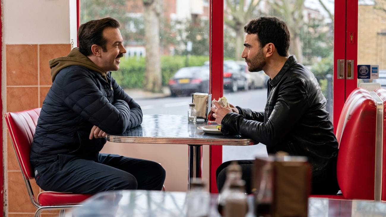 Two men face each other in a cafe.