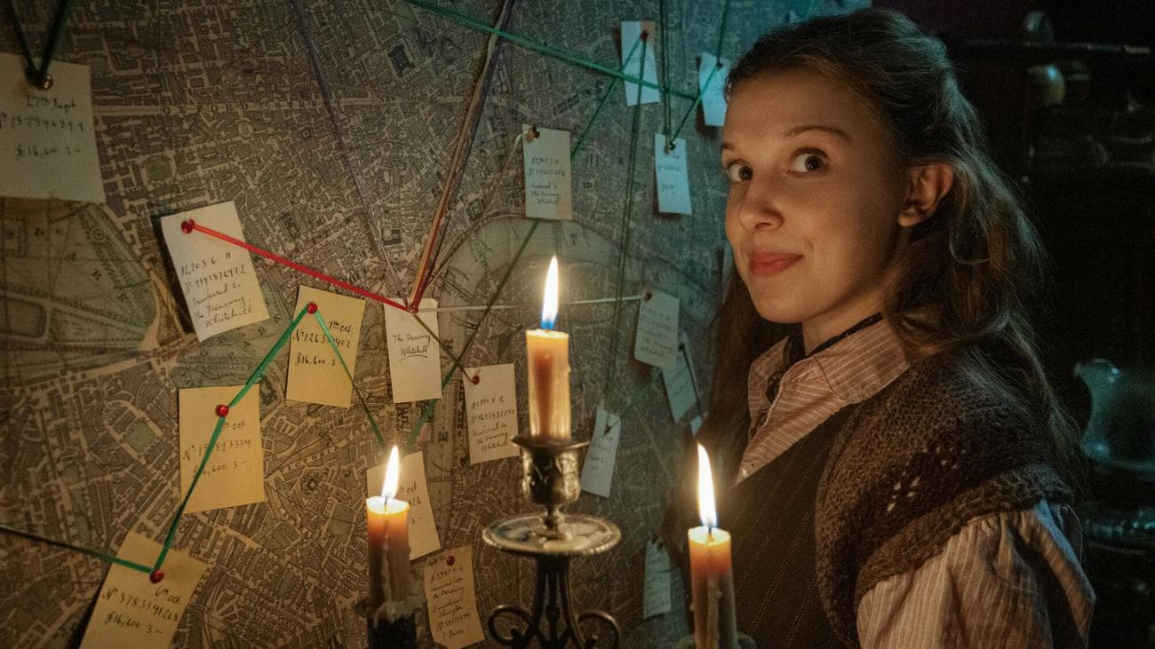 Millie Bobbie Brown stands by a red yarn wall with a candelabra in the film 