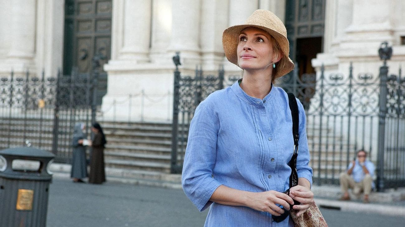 A woman wearing a blue shirt and sun hat walks in a city. 