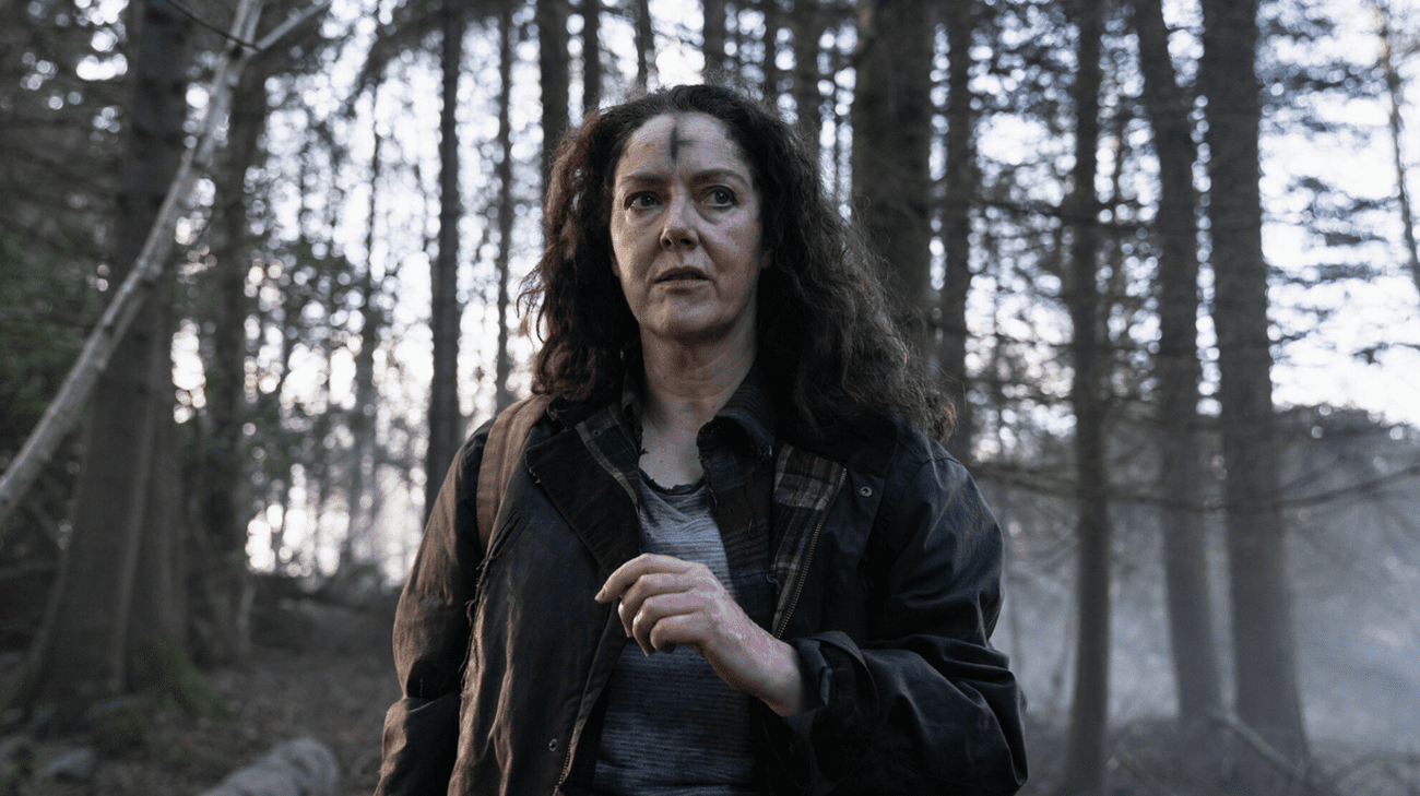 A woman walks through the woods with a black cross daubed on her forehead.