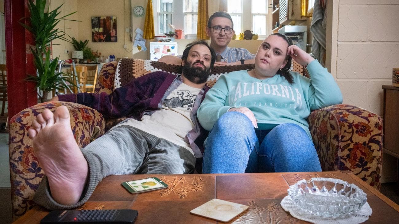 Tim Renkow, Sharon Rooney, and Rob Madin sit together posed on the couch in "Jerk."