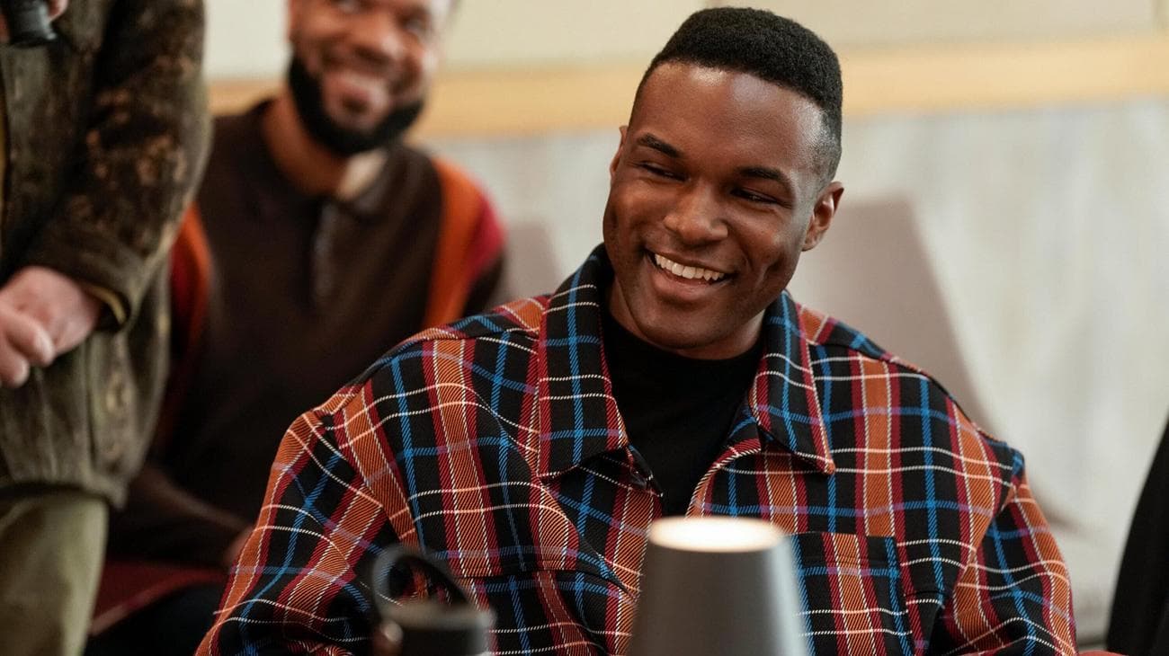 A young man wearing a plaid shirt laughs during a table read. 