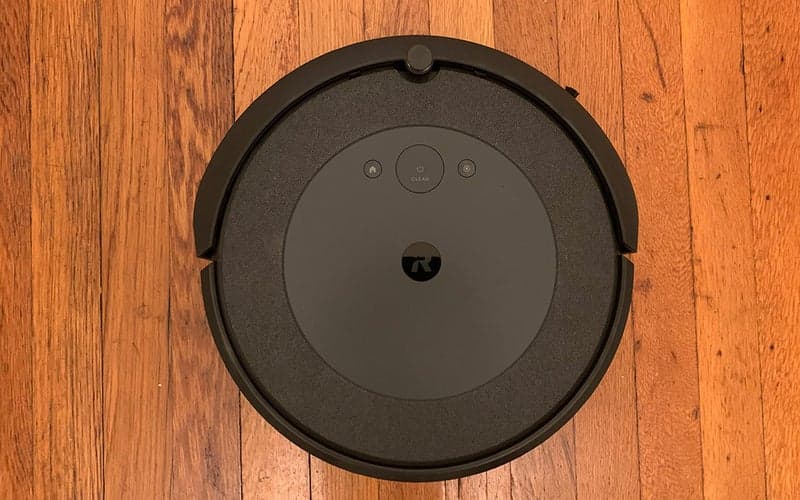A round black iRobot Roomba i4 against a wooden floor.