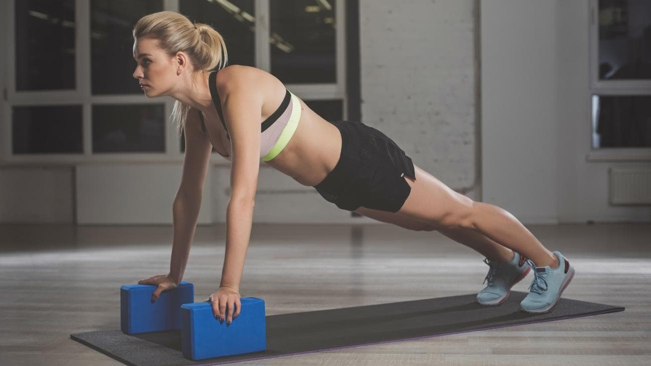 Γυναίκα σε θέση push-up με τα χέρια σε μπλοκ γιόγκα