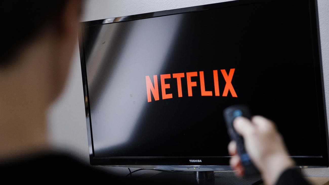 Ένας άντρας παρακολουθεί το λογότυπο του Netflix σε μια τηλεόραση Toshiba με ένα τηλεχειριστήριο στο χέρι
