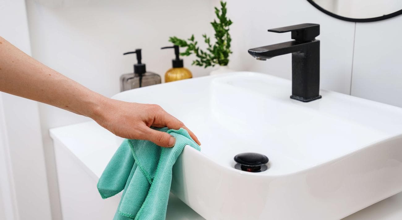 Γυναίκα που καθαρίζει έναν νεροχύτη μπάνιου με ένα πανί μικροϊνών