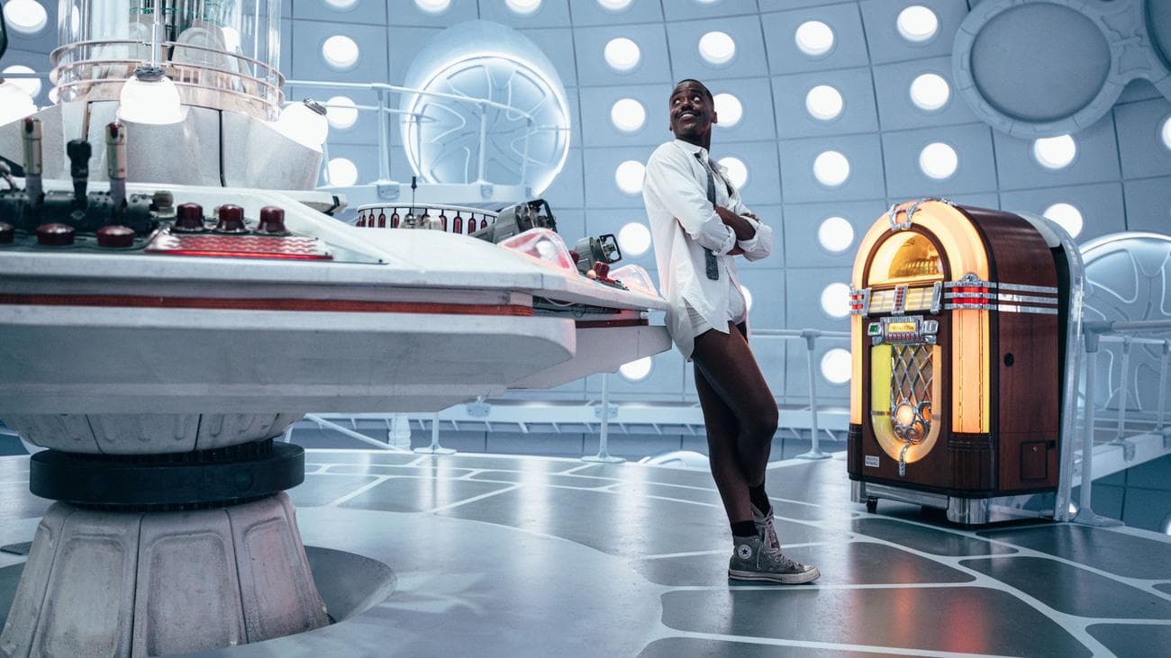 Doctor Who leans against the control panel of the TARDIS.