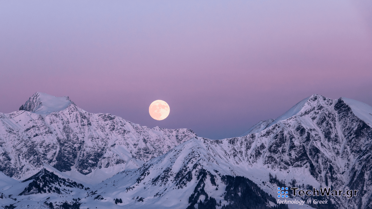 A full moon rises n a purple sky over snowy mountain peaks.
