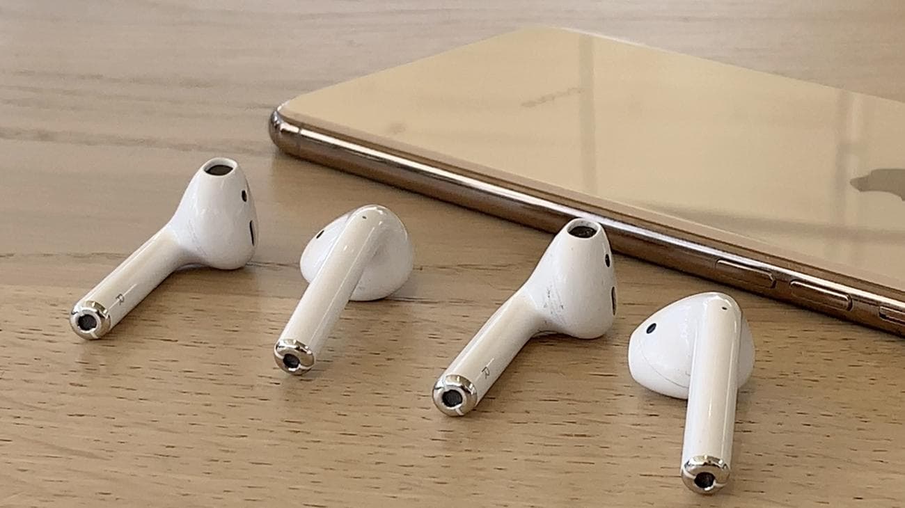 AirPods 2 και AirPods 1 δίπλα σε ένα iPhone X σε ένα ξύλινο τραπέζι