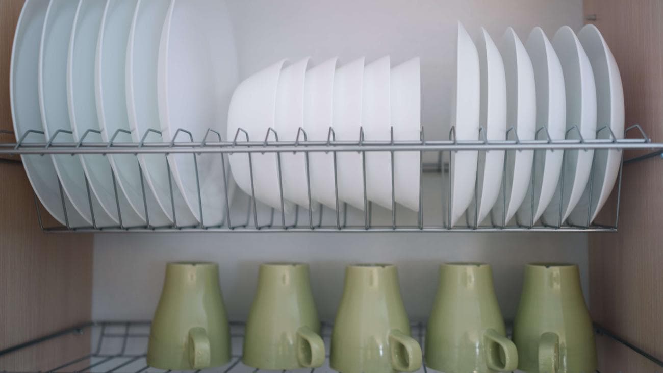 Πιάτα και κούπες αποθηκευμένα σε συρμάτινα ράφια στο ντουλάπι της κουζίνας