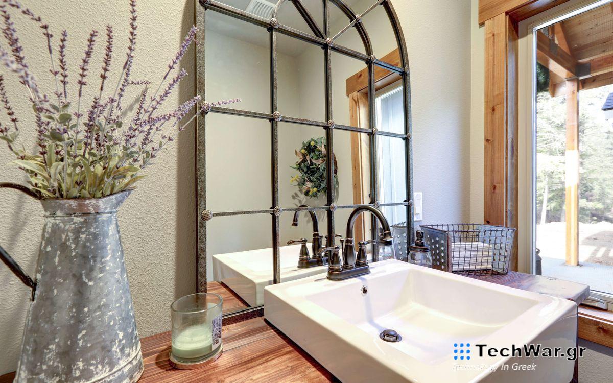 Arched mirro over a square white bathroom sink, with a metal jug of lavender