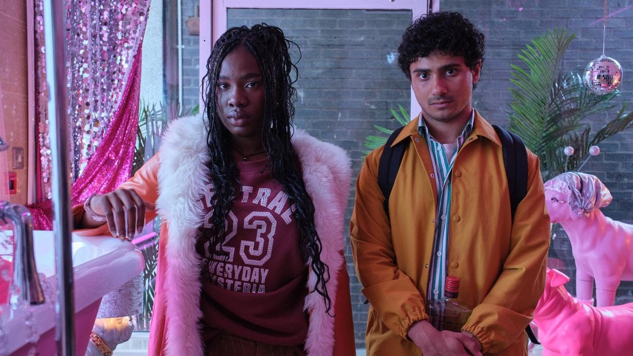 Η Vivian Oparah και ο Bilal Hasna στέκονται σε ένα έντονο ροζ σαλόνι περιποίησης σκύλων.