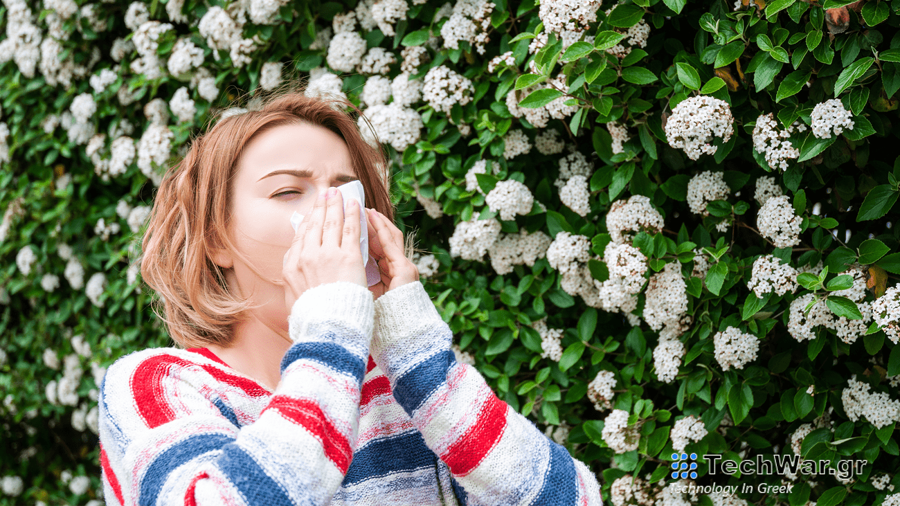 a women blows her nose into a facial tissue while standing next to blooming white flowers